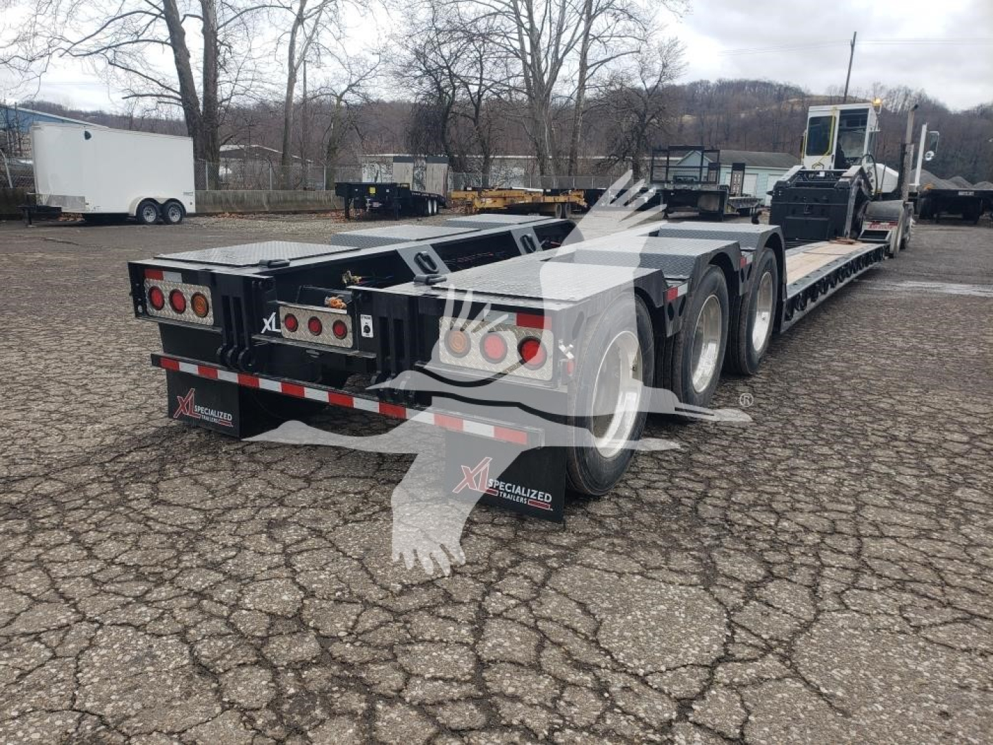XL Specialized 55 Ton 15" Deck Height lowboy trailer showing dual rear ramps and wheel covers with multiple axles and taillights.