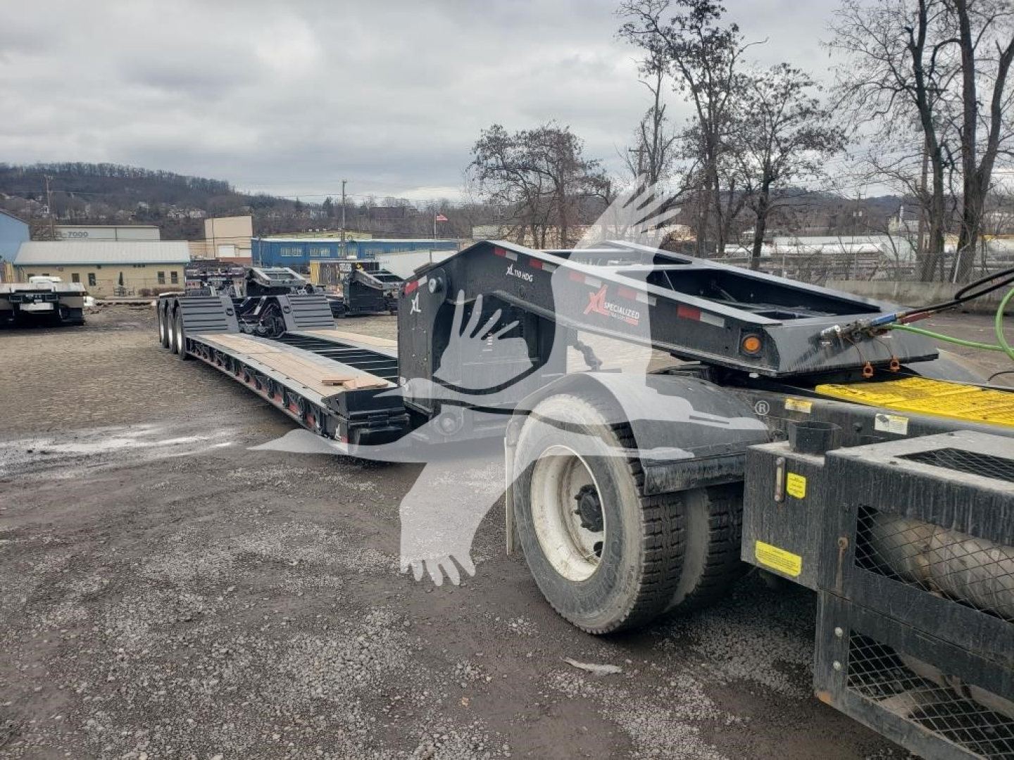 Lowboy trailer with 55 ton capacity, 15 inch deck height, wheel covers visible; side view showing hydraulic ramps and large tires; branding reads XL Specialized.