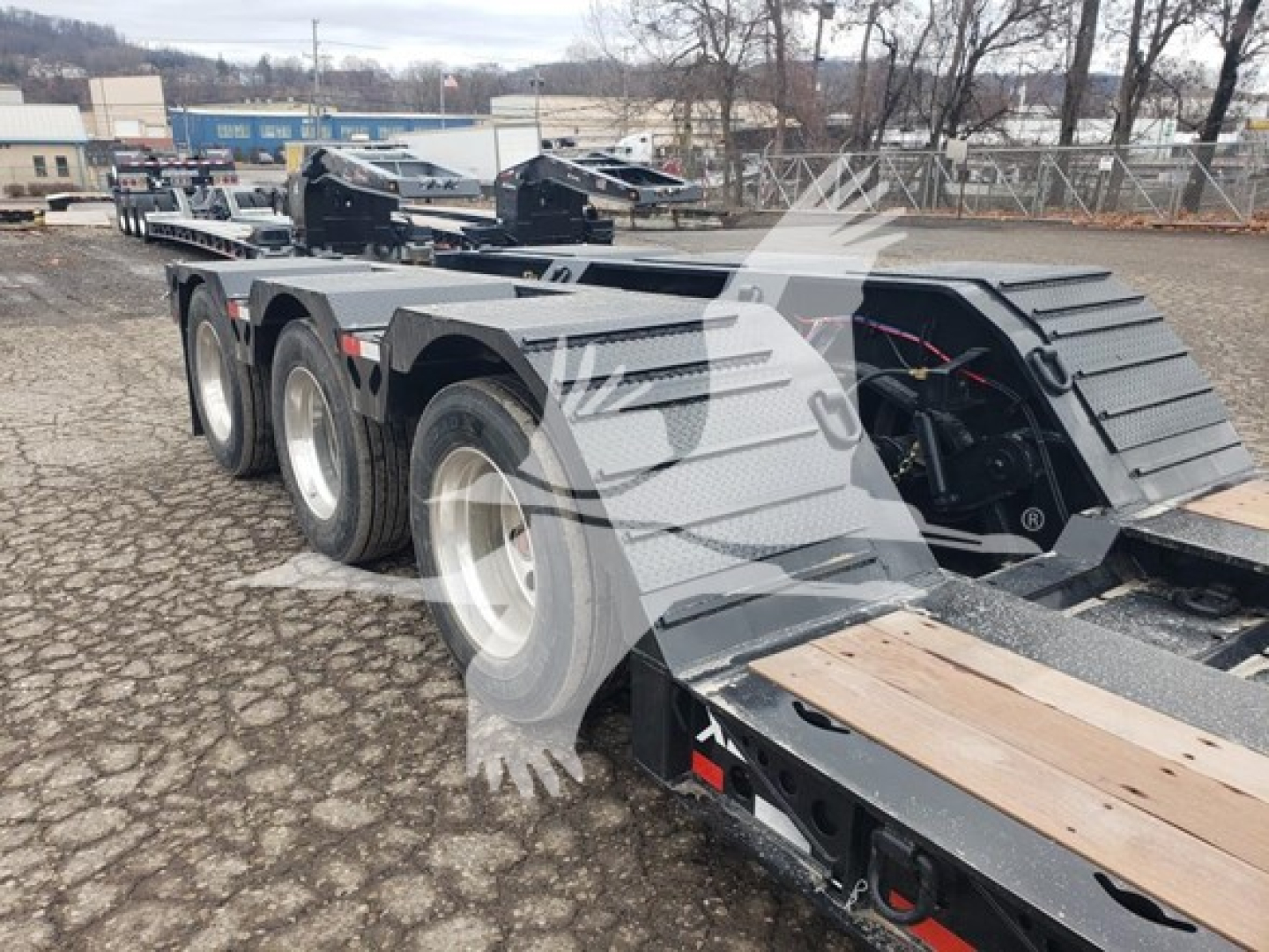 35-foot lowboy trailer with triple-axle rear, dual tires, and a dedicated toolbox area; metal deck with wooden boards and ramp sections, light gray paint.