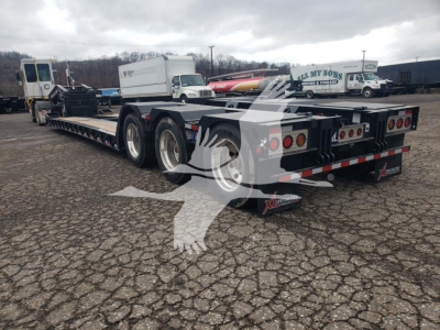 Trailer showing a 55-ton lowboy with dual rear axles and wheel covers; visible labels include XL Specialized 55 Ton 15" deck height; rear lights, reflective tape, and VIN/stock decals on side.