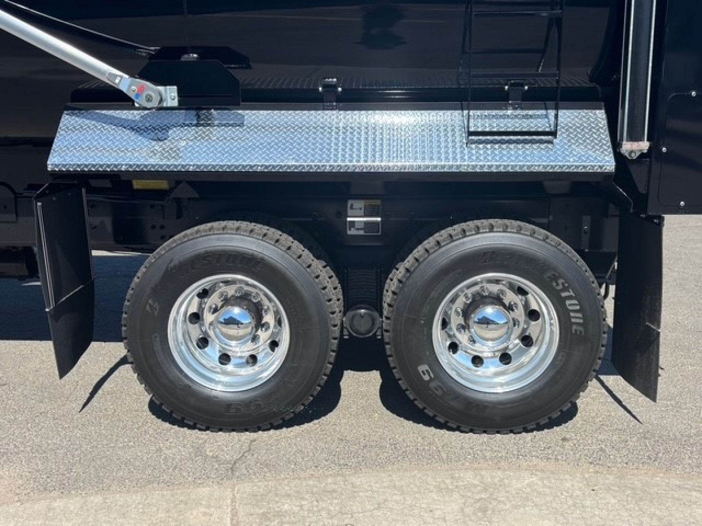 Dual rear wheels on a Mack GR64F dump truck showing polished rims, heavy-duty diamond plate toolbox and fender area.