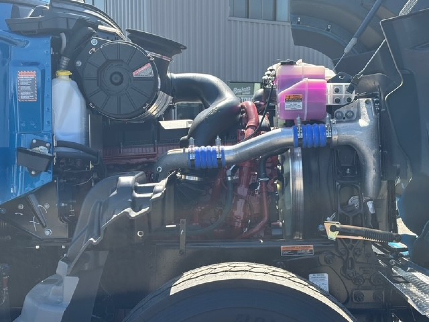 Mack GR64F engine bay showing turbocharger and intercooler piping, coolant reservoir, and auxiliary components in view.