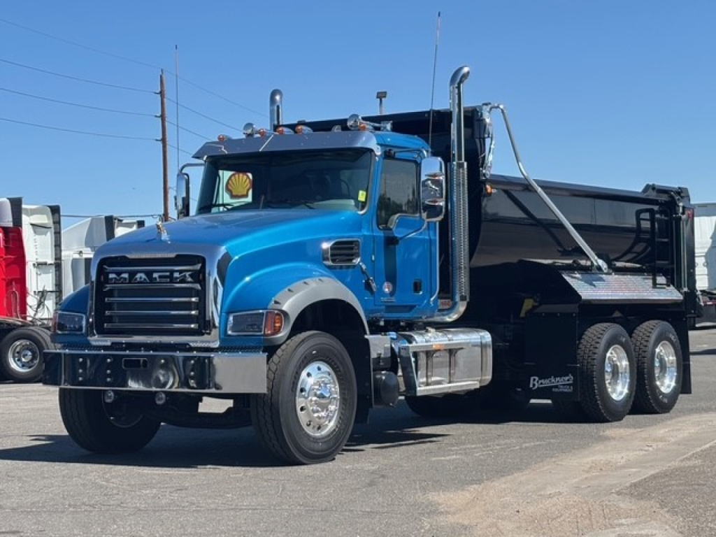 Blue Mack dump truck with large grille and stacked exhaust stacks, showing Mack branding on the grille and a black dump bed.
