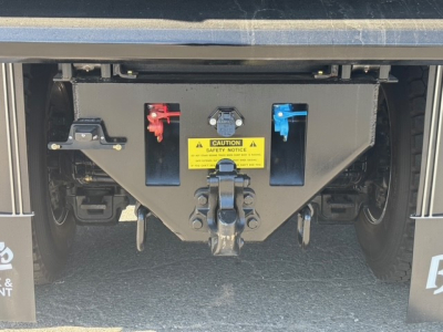Dump truck hitch area with black metal block and red and blue hydraulic connections, warning label, and coupling hook visible.