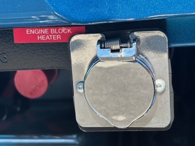 Mack GR64F engine area showing Engine Block Heater label and circular fuel/auxiliary cap with metal mounting plate.