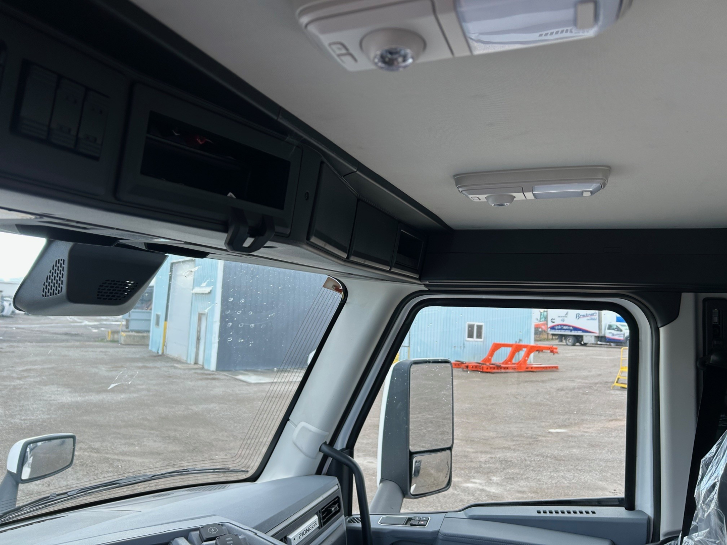 Cab interior of a 2026 Mack PR64T truck showing overhead console, sun visor, ceiling light, and driver side window with mirror.