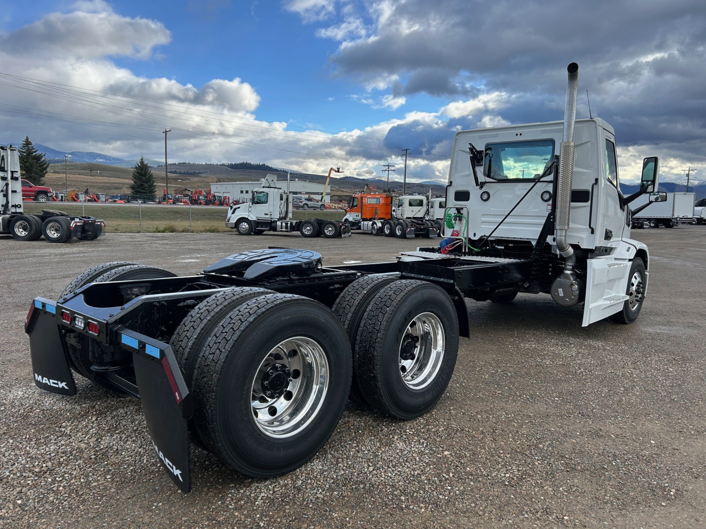 Mack PR64T conventional daycab tractor chassis rear view showing dual rear axles and fifth-wheel area, white cab, gravel lot.