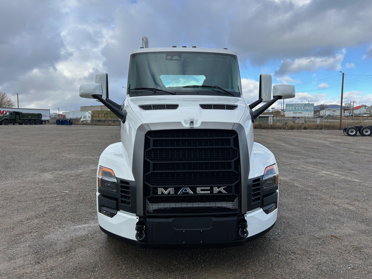 Front view of a white 2026 Mack PR64T truck cab showing bold black grille with MACK lettering, large bumper, dual mirrors, and hood vents.