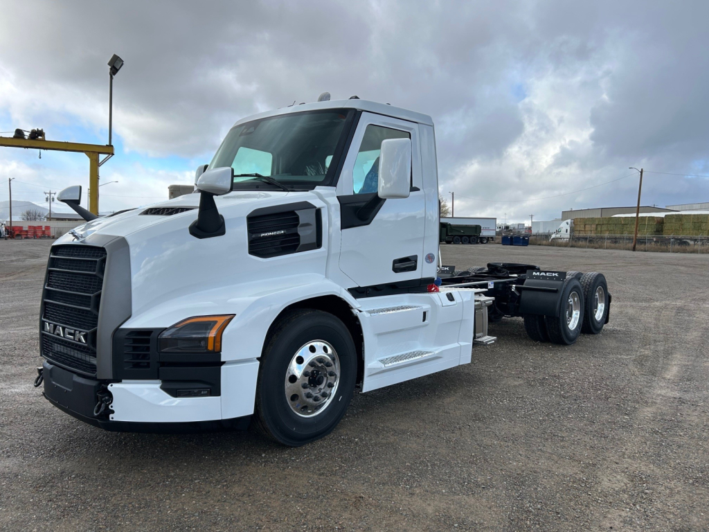 White Mack PR64T truck chassis side view showing front grille with Mack emblem, cab with black mirrors, and dual rear axles; no visible text except truck styling.