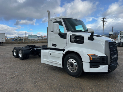 Truck side view of a white 2026 Mack PR64T conventional daycab with three-axle configuration, showing cab, fuel tanks, and chassis