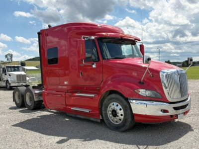 Truck cab showing International ProStar122 Premium sleeper tractor in red with attached trailer chassis visible, side view.