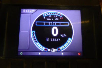 Calibrated digital gauge display showing 0 mph and rpm x100 with circular dial, time 8:57am, and various indicator bars.