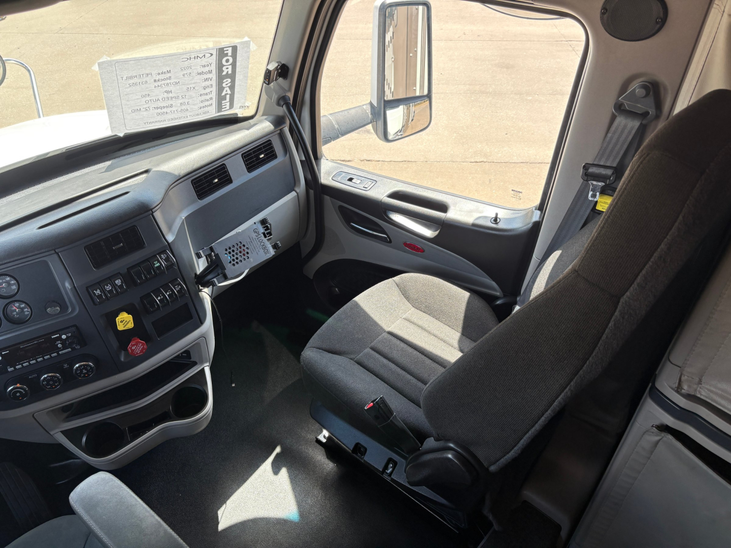 Peterbilt 579 truck interior cabin view from the driver side showing dash controls, steering wheel, and grey fabric seat.