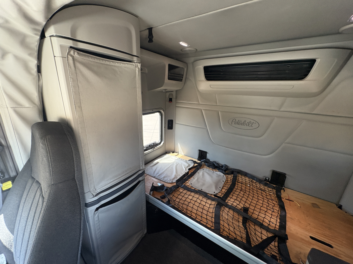 Peterbilt 579 sleeper cab interior with bunk area and storage netting seen from passenger side, white interior panels and overhead storage.