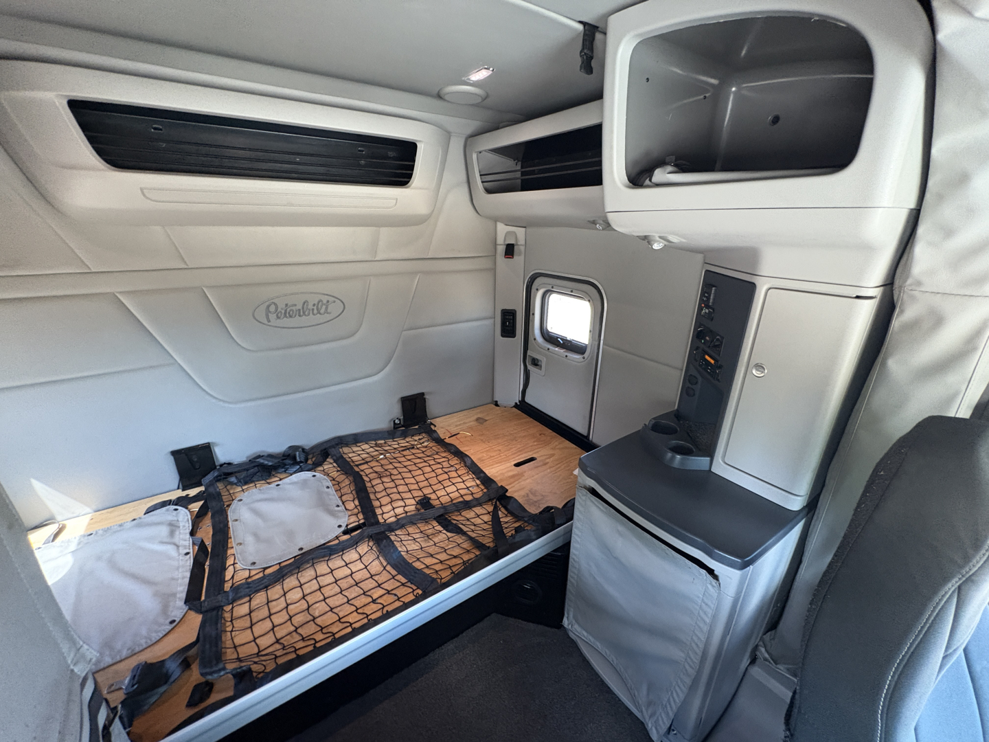 Peterbilt 579 sleeper cab interior showing cargo bed with straps and storage cabinet and side window.