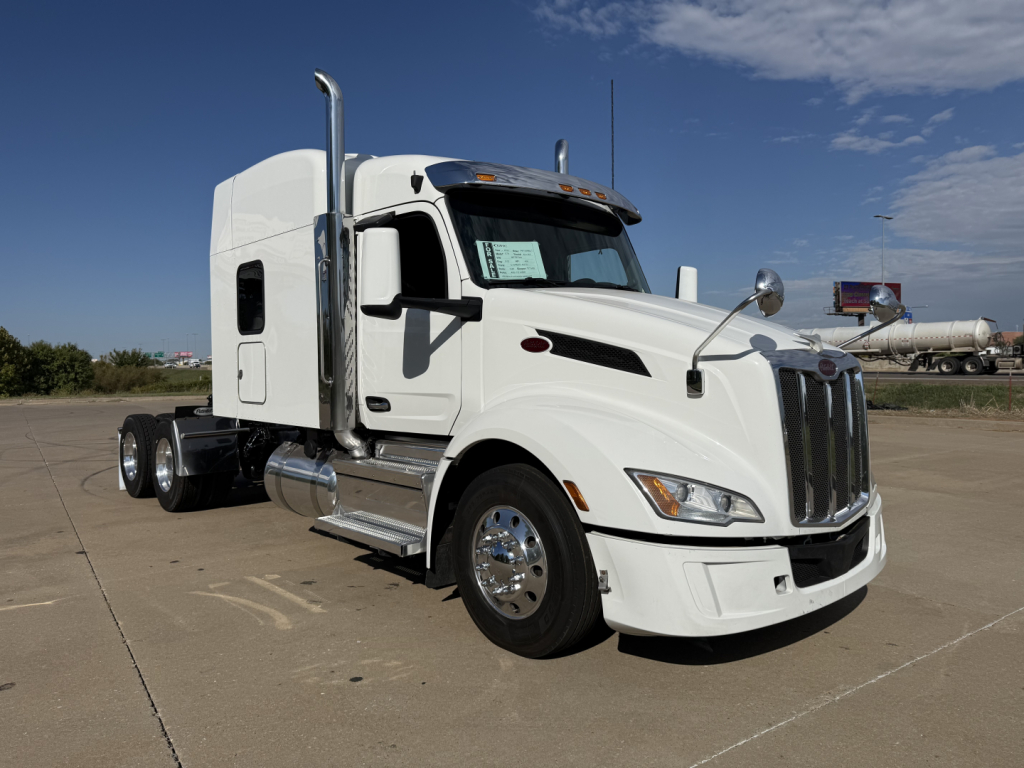 Peterbilt 579 semi-truck in white, side view showing sleeper cab, chrome exhaust stacks, dual rear axles, and aerodynamic front with grille.