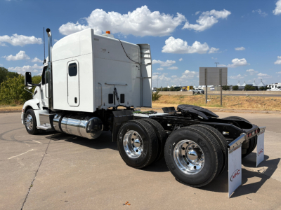 Peterbilt 579 conventional sleeper tractor rear view showing dual rear axles and chrome wheels, white cab, fuel tanks, and fifth wheel.
