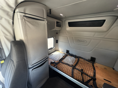 Peterbilt 579 sleeper cab interior with bunk area and storage netting seen from passenger side, white interior panels and overhead storage.