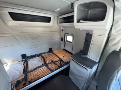 Peterbilt 579 sleeper cab interior showing cargo bed with straps and storage cabinet and side window.
