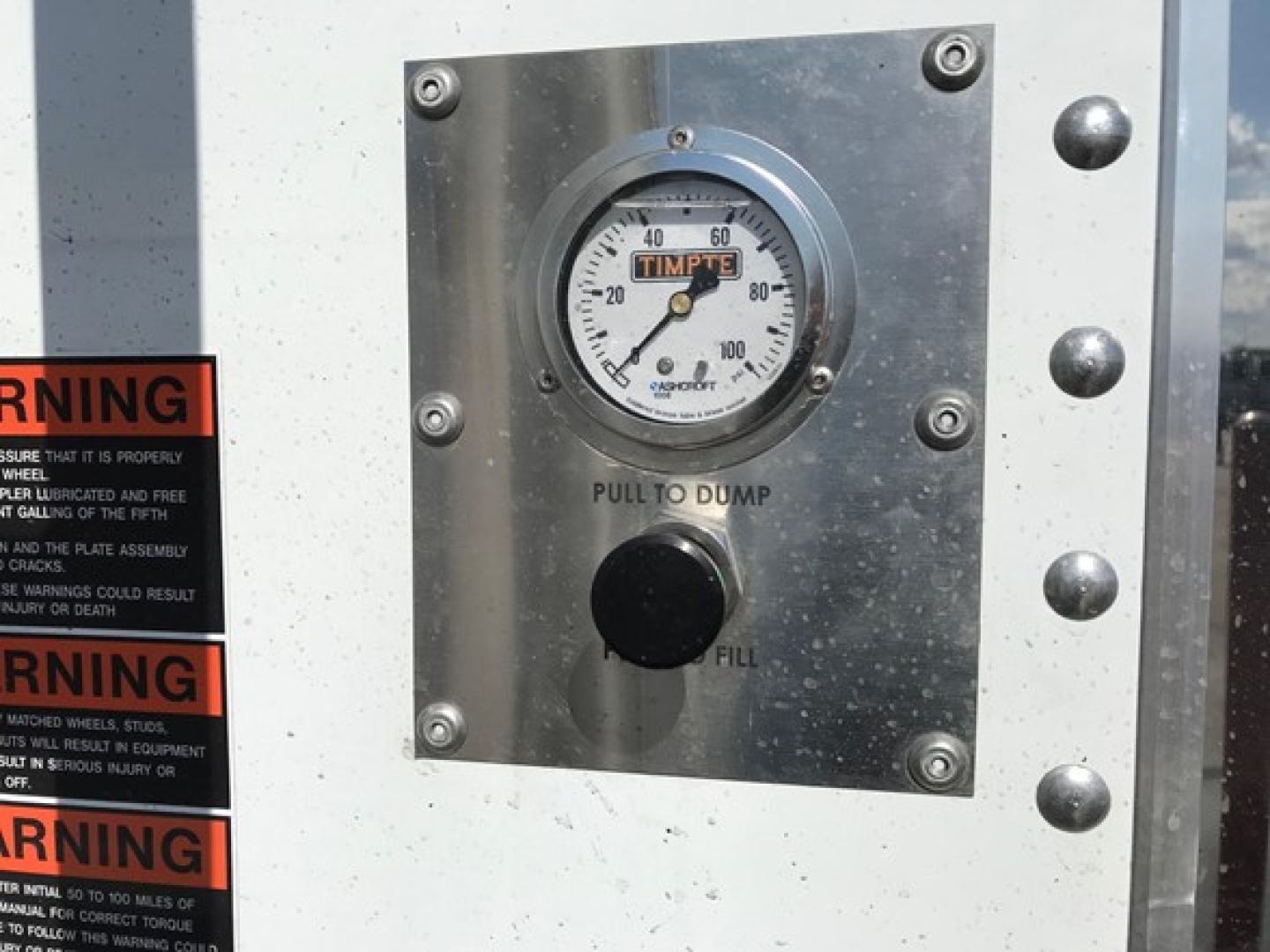 Timpte Super Hopper trailer control panel with dial gauge labeled TIMPTE and pull to dump / fill button. Warning stickers visible on left.