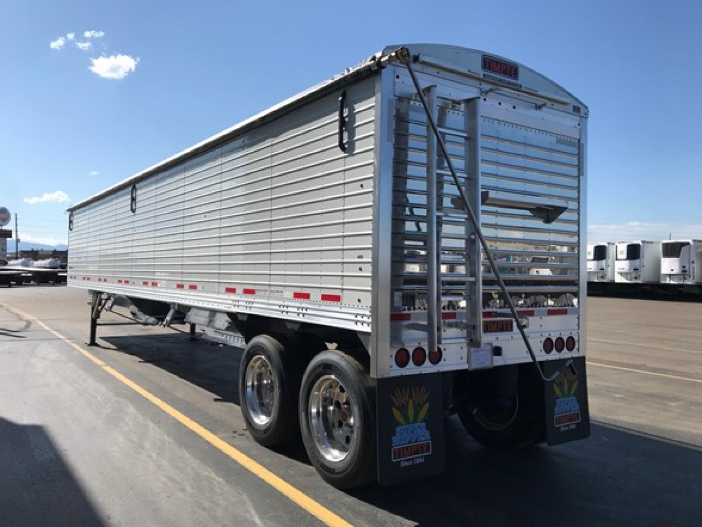 Timpte Super Hopper trailer showing riveted aluminum side panels, dual rear doors, and tandem axles with aluminum wheels in a dealership lot.