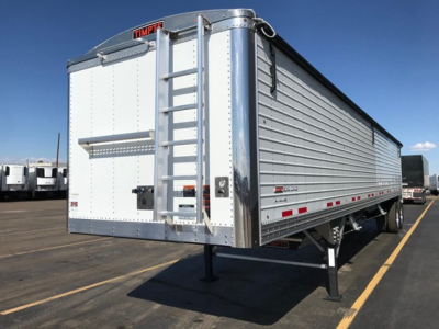 Timpte Super Hopper trailer with ladder and rear doors, aluminum body, dual rear legs, in a dealership lot. Visible branding reads Timpfe on rear.