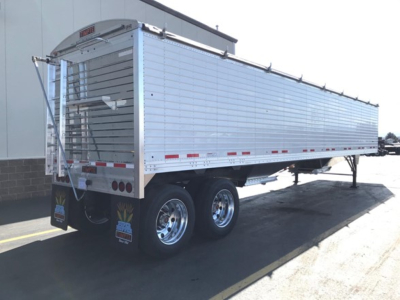 Trailer side view showing Timpte Super Hopper with dual rear axles, aluminum exterior, rear access ladder, multiple reflective tape strips, and mud flaps.