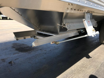 Trailer undercarriage showing underside of hopper with metal framework, hydraulic or lift components, and a white hydraulic cylinder mount.