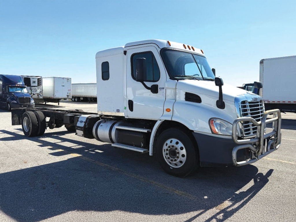 Truck cab and chassis showing Freightliner Cascadia daytime running lights and front grille with bumper guard. White sleeper cab with side mirrors and twin fuel tanks.