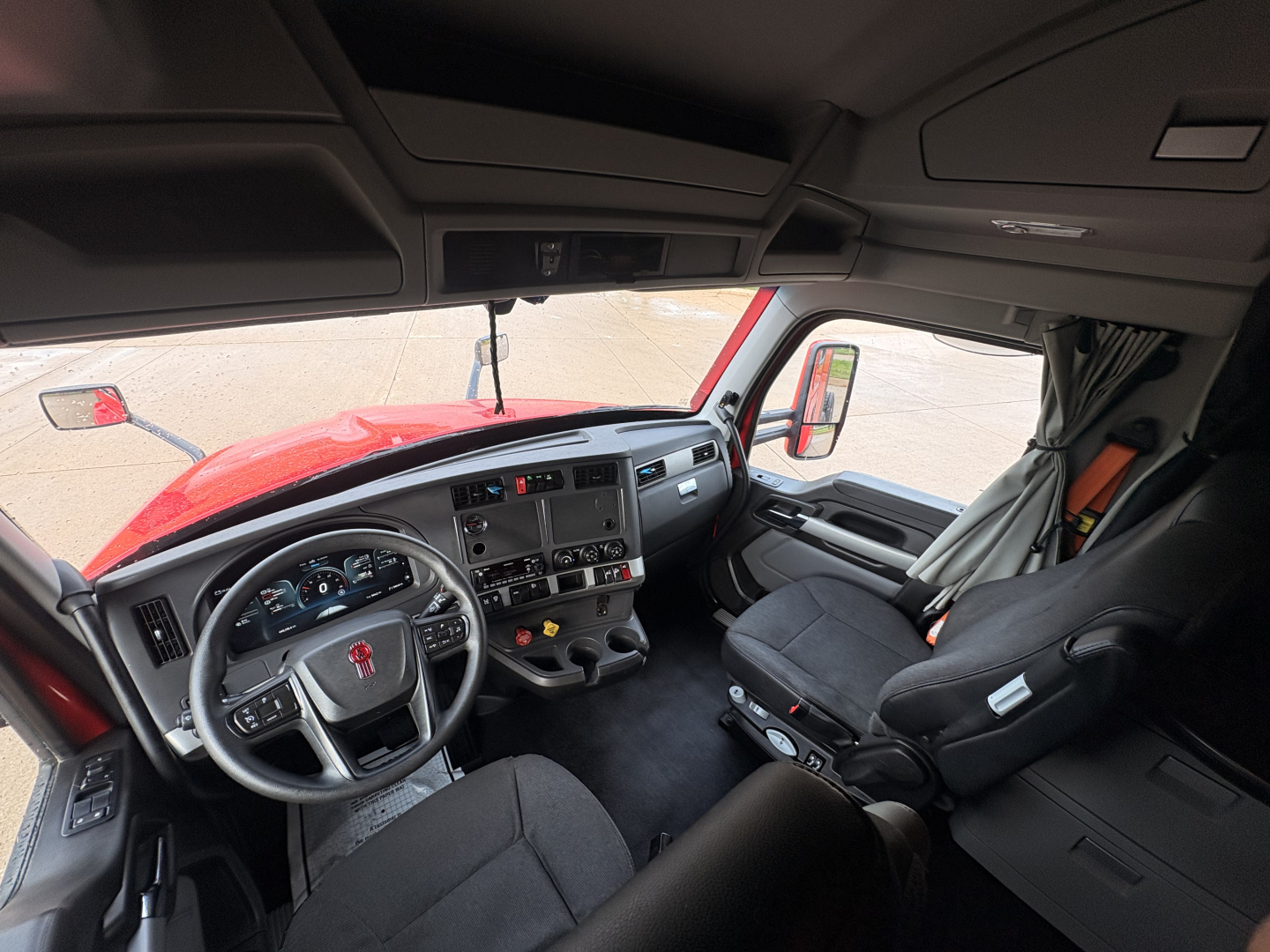 Truck cab interior of a 2022 Kenworth T680 showing steering wheel, dashboard, and driver seat from passenger side. Visible labels: none.