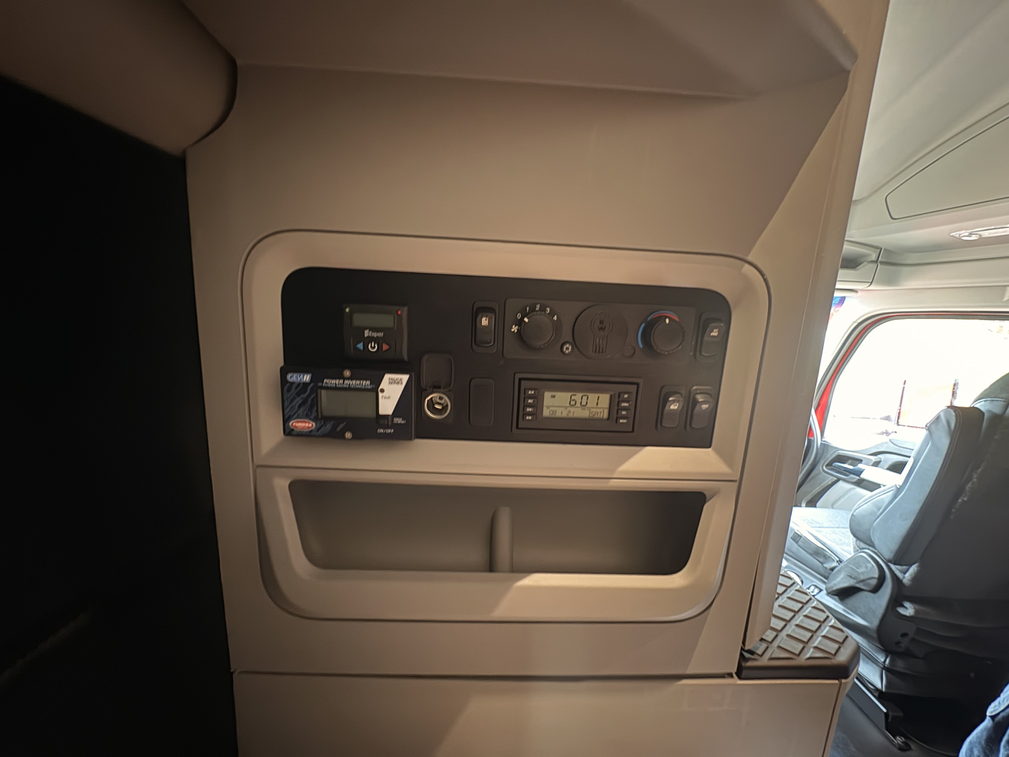 Kenworth T680 cab interior panel showing control switches, displays, and storage pocket near driver seat.