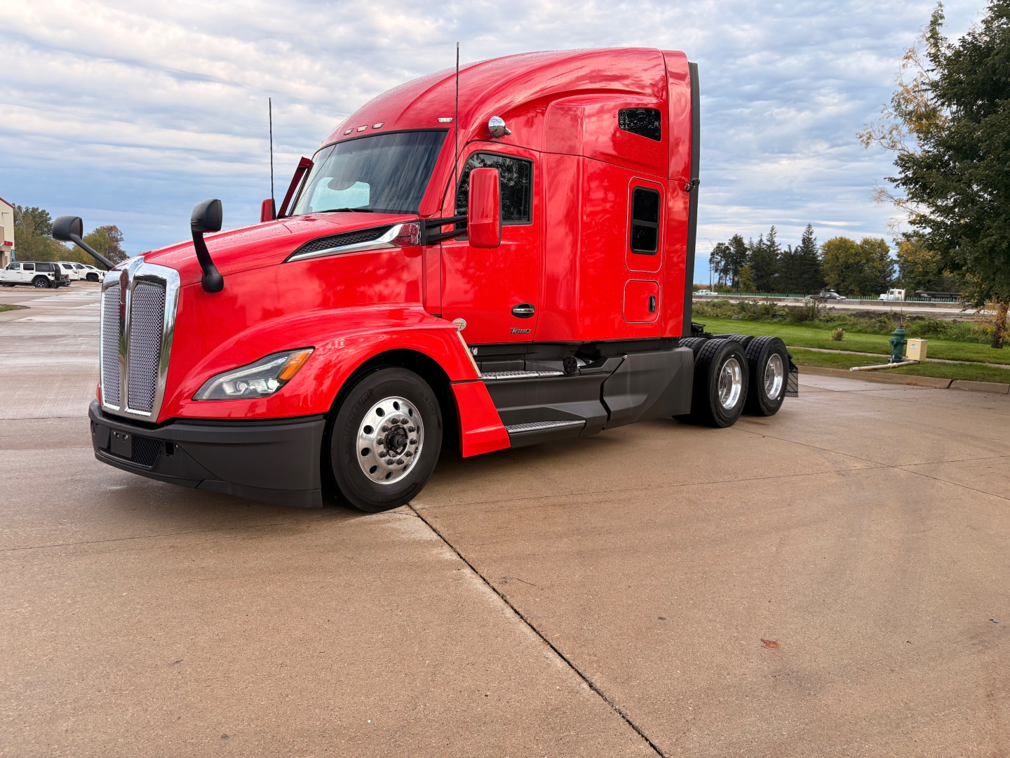 Kenworth T680 tractor-trailer in red, left front angle showing cab, grille, and dual rear axles with chrome wheels; no visible text legible on image.