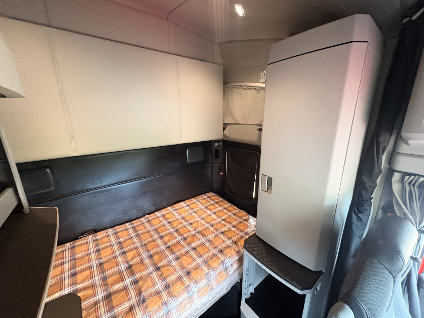 Kenworth T680 sleeper cab interior showing bunk bed with plaid bedding and overhead storage compartments.