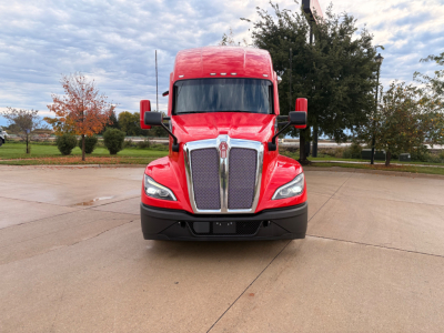 Kenworth T680 front view with red cab and chrome grille, head-on in parking lot.
