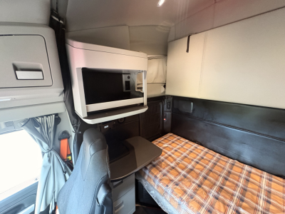 Kenworth T680 sleeper cab interior showing overhead microwave, storage cabinet, and plaid sleeper mattress.