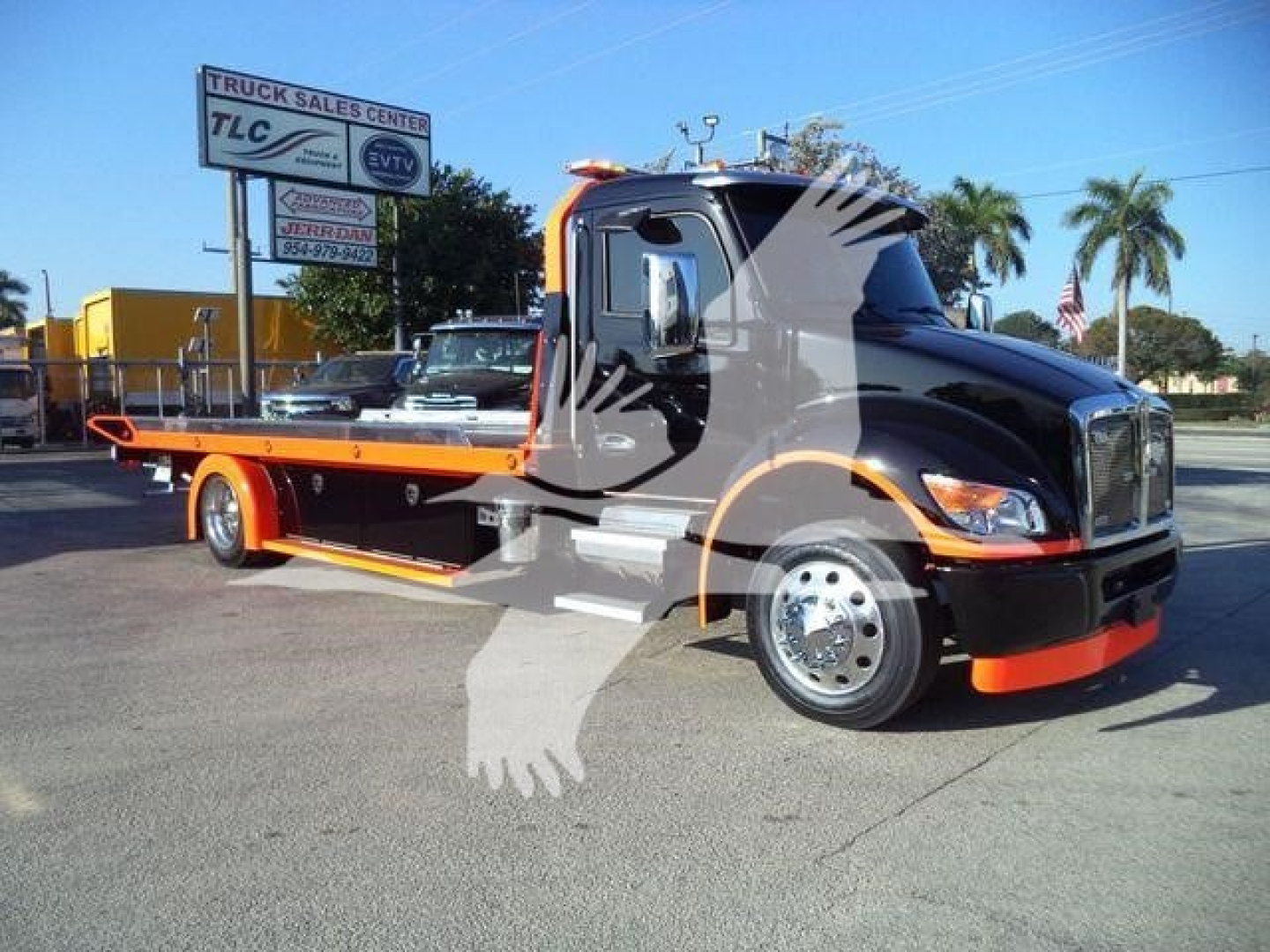 Kenworth T280 rollback tow truck in black and orange livery with company sign in background.