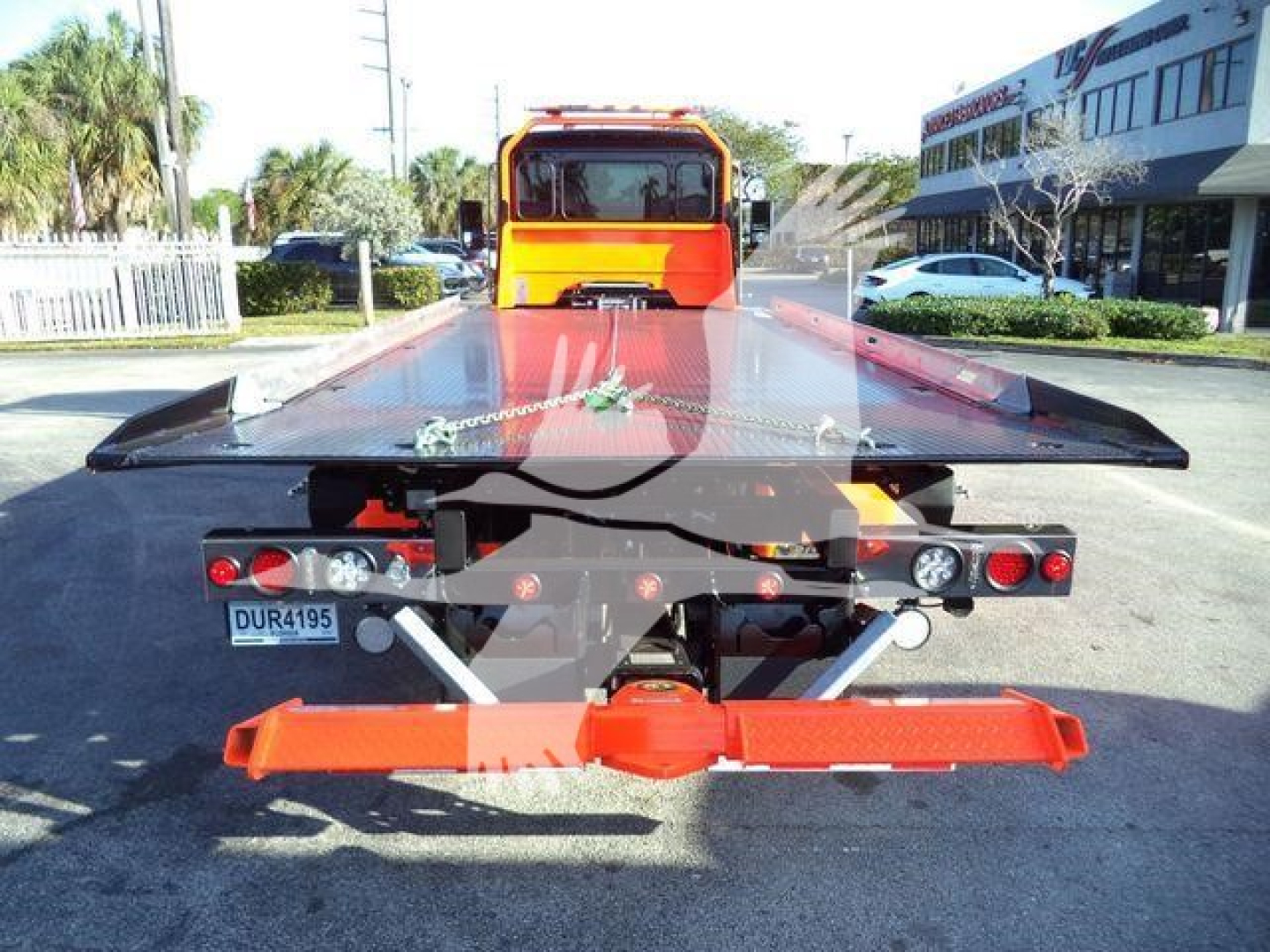 Kenworth T280 rollback tow truck rear view with flatbed and ties, orange hydraulic components, rear lights, and license plate visible.