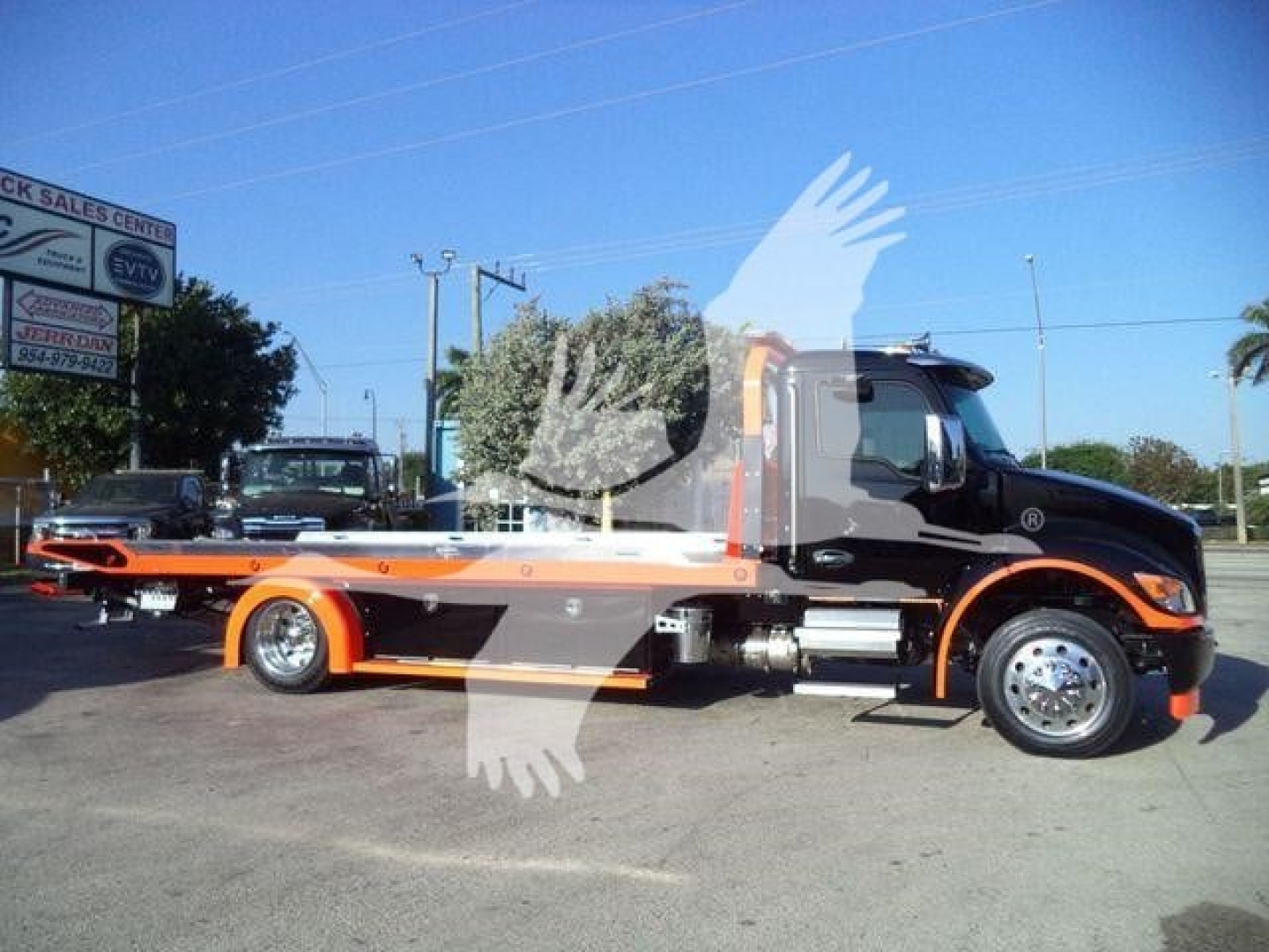 Kenworth T280 rollback truck in side profile view with black and orange livery, flatbed with wheel lift, dealership lot in background.