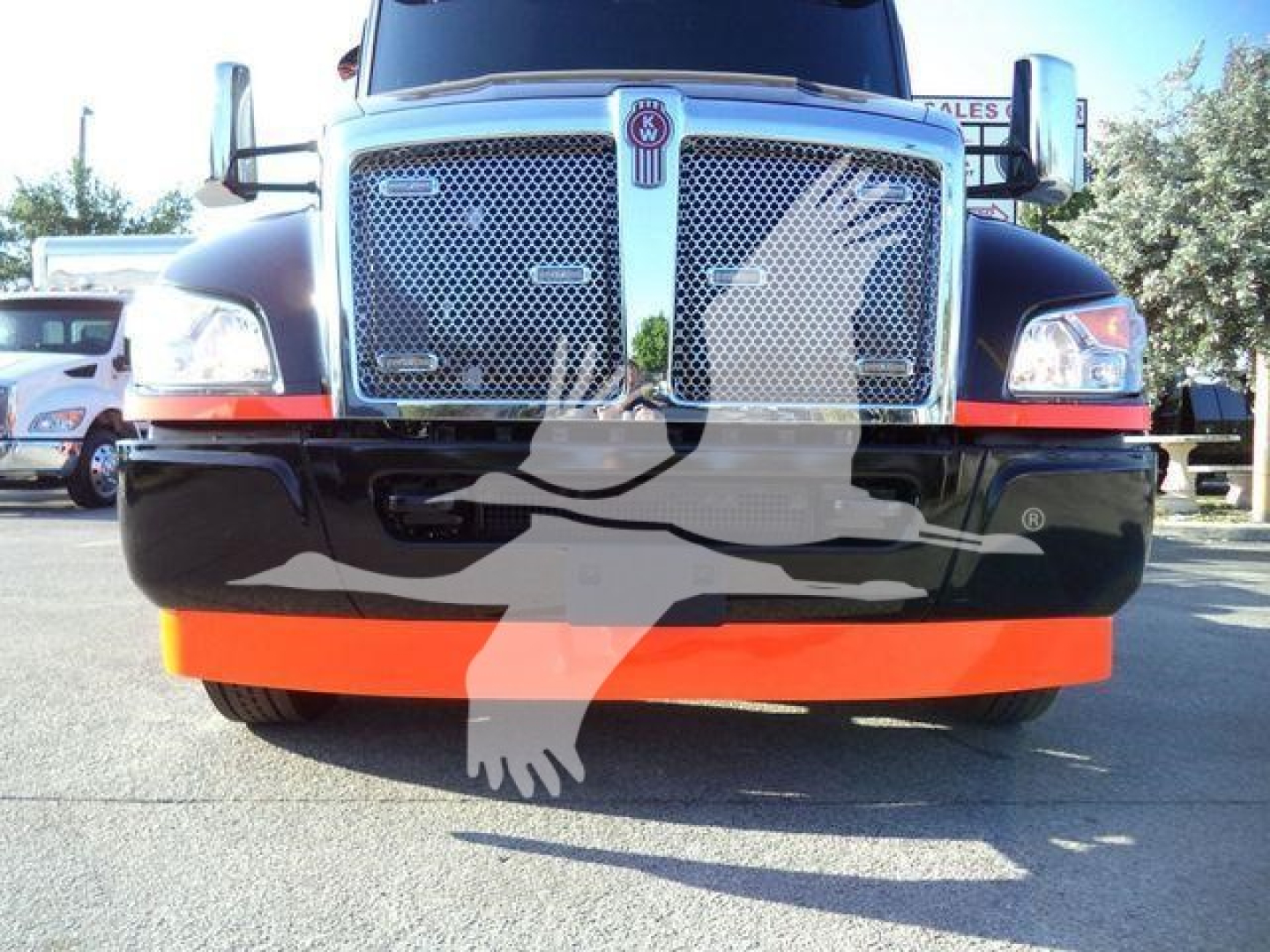 Kenworth T200 series front view showing large chrome grille, emblem, headlights, and orange bumper protector on a black lower fascia.