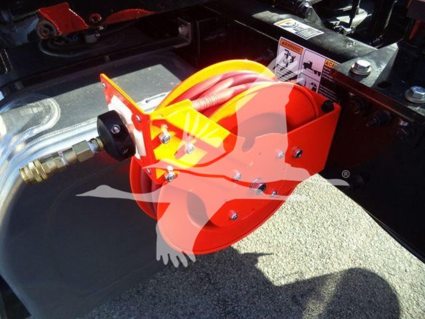 Kenworth truck bed area showing a bright orange hitch device with a hydraulic hose and connector mounted near the frame.