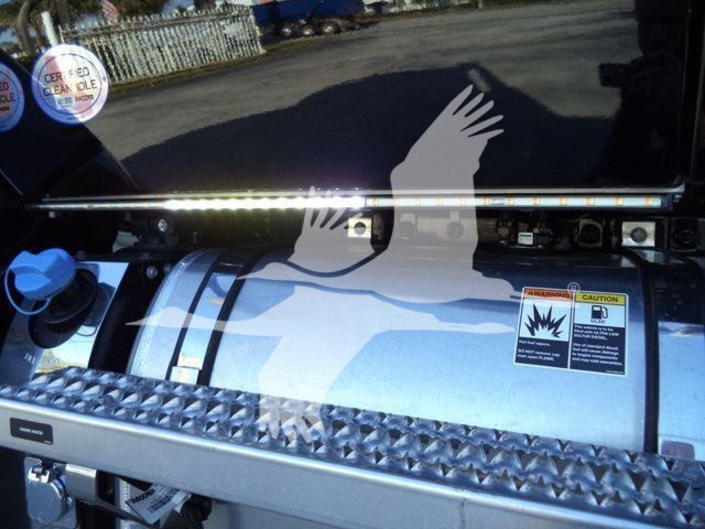 Roll back truck fuel tank area with diamond plate step, warning label, and chrome bar; visible text includes caution label and blue cap.