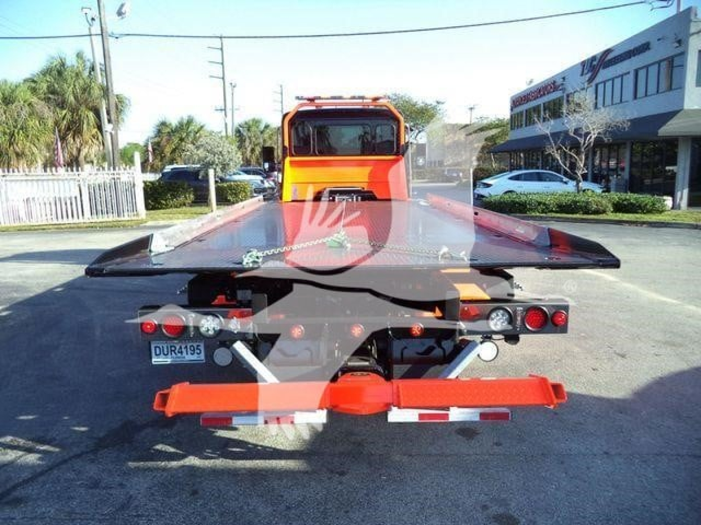 Back view of a bright orange Kenworth rollback tow truck with a flatbed loaded, license plate visible, in a dealership lot.