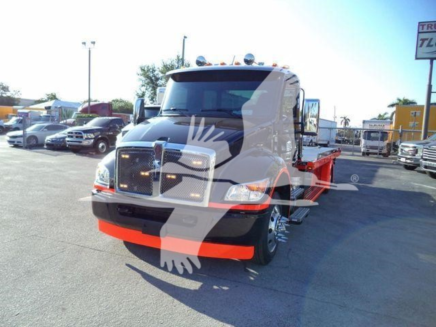 Truck front view of a new 2025 Kenworth T280 rollback wrecker body in a dealership lot with chrome grille and orange chassis accents.