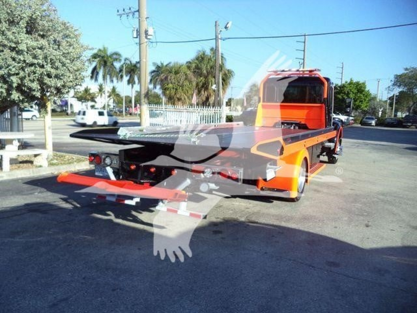 Kenworth T280 rollback tow truck rear view showing vibrant orange body and flatbed at a sunny lot.
