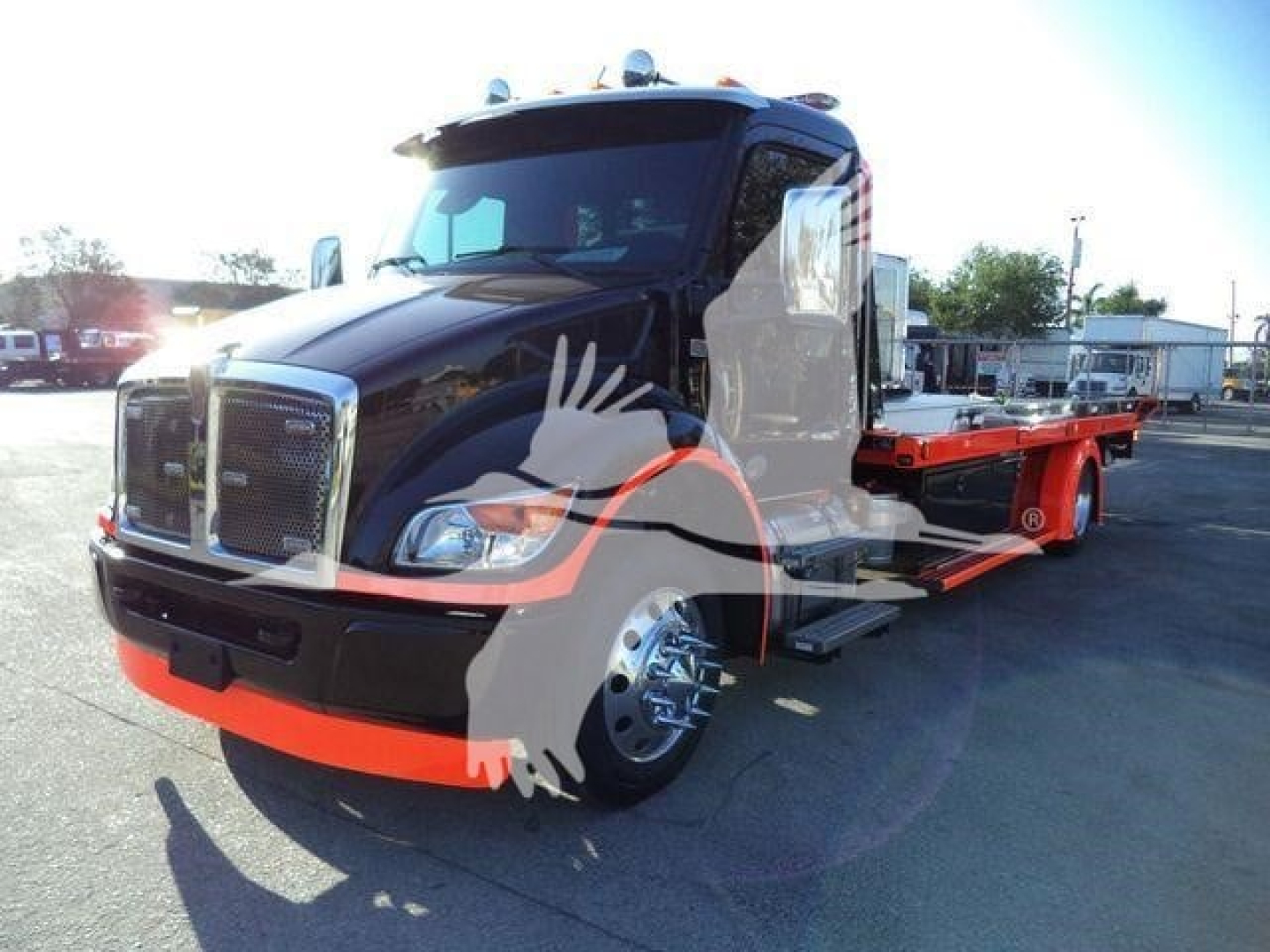 Kenworth T280 rollback tow truck in black with orange chassis rails, front grille and bumper; side view showing dual rear wheels and flatbed