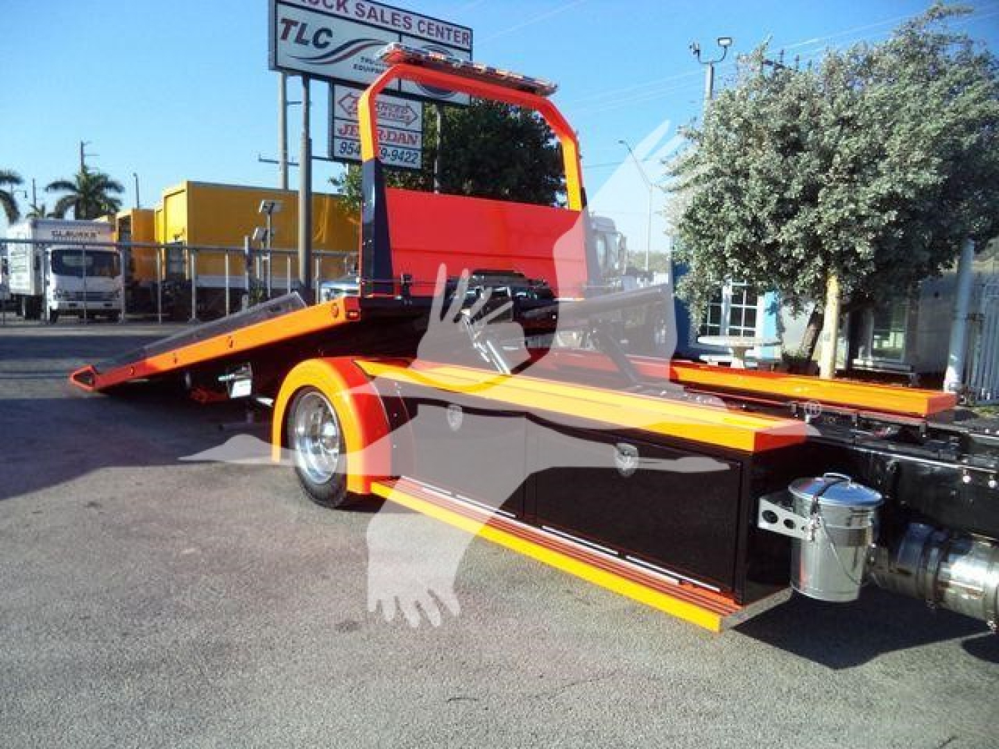 Kenworth T280 rollback truck on a lot showing a flatbed with bright orange and black color scheme and red roll bar.