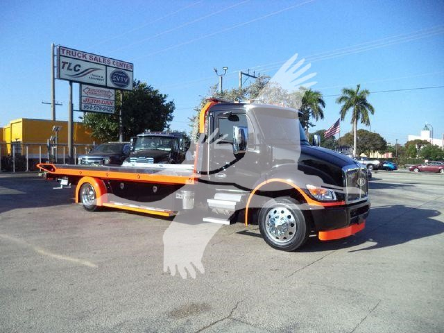 Kenworth T280 rollback truck in a dealership lot with orange-and-black color scheme, long flatbed, front grille, and side mirrors visible.