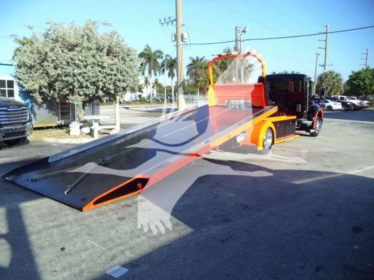 Truck bed with a lowered ramp on a Kenworth T280 rollback, orange and black color scheme, front cab visible in background.