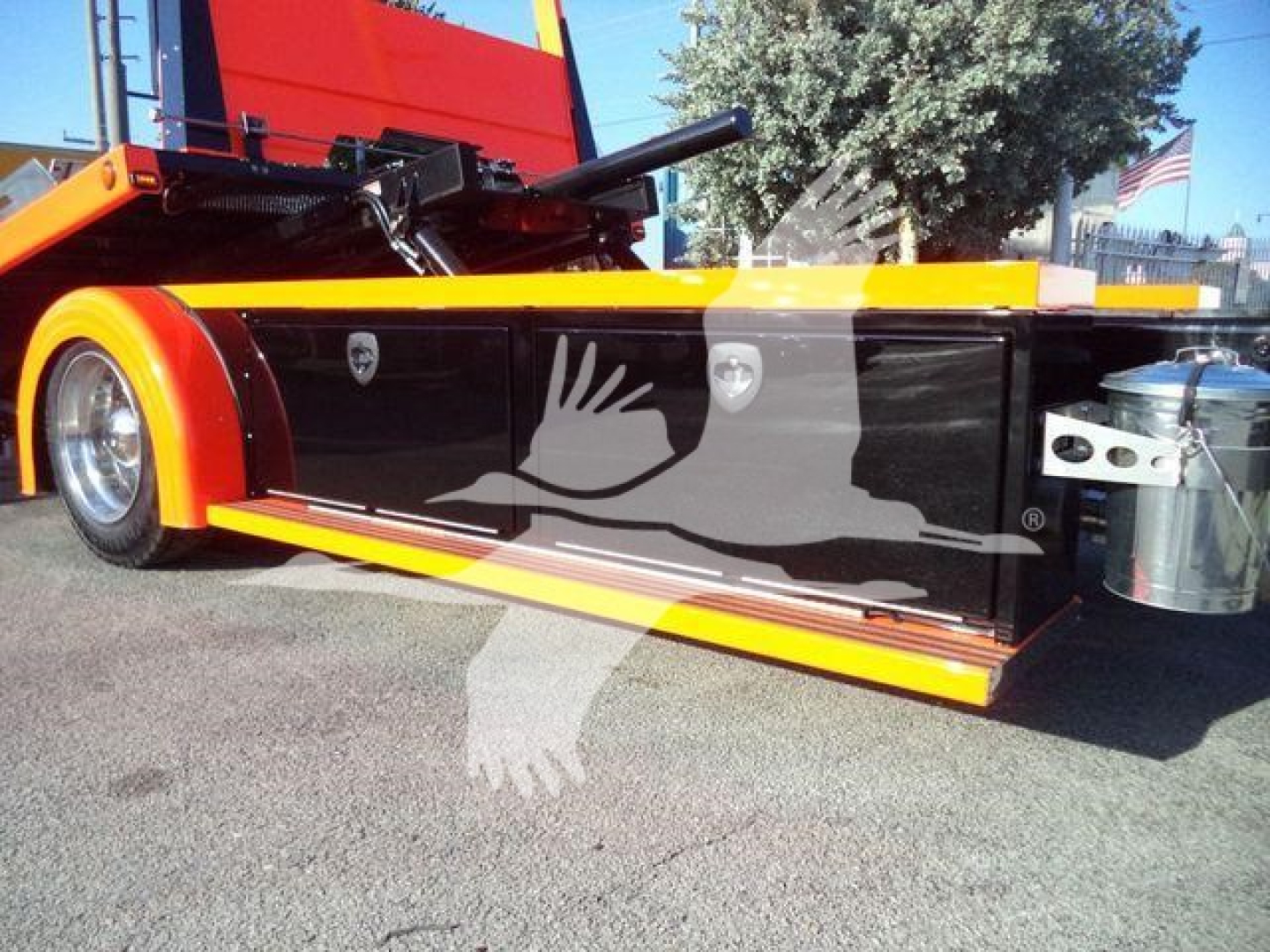 Kenworth T280 rollback truck side view showing black side panel with white graphic and yellow accents, storage box and chrome wheel; rear hitch and hydraulic components visible.