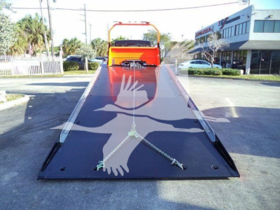 Tow truck rollback bed with orange cab back and flat steel ramp, two chains secured across the platform, reflective gloves logo overlay.